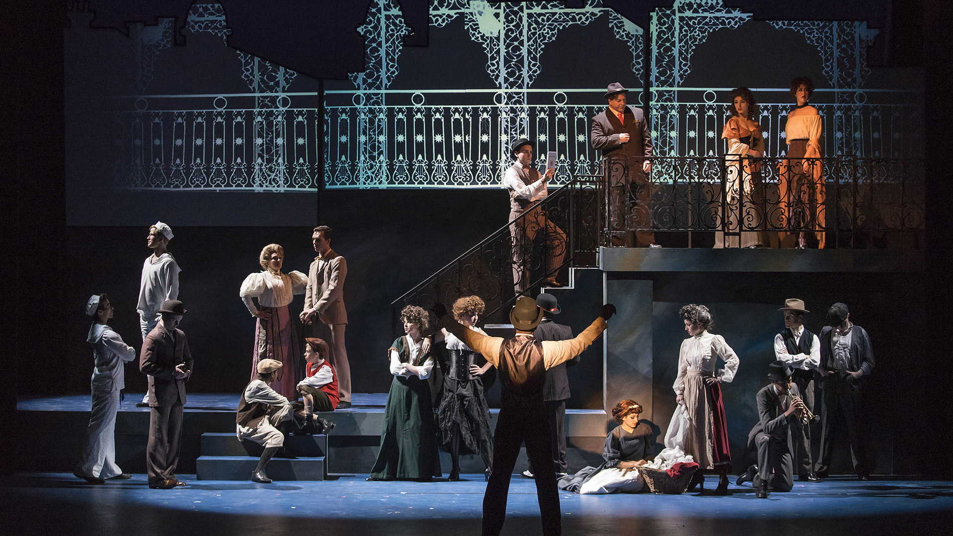 A large cast arranged across the stage with an iron work balcony.